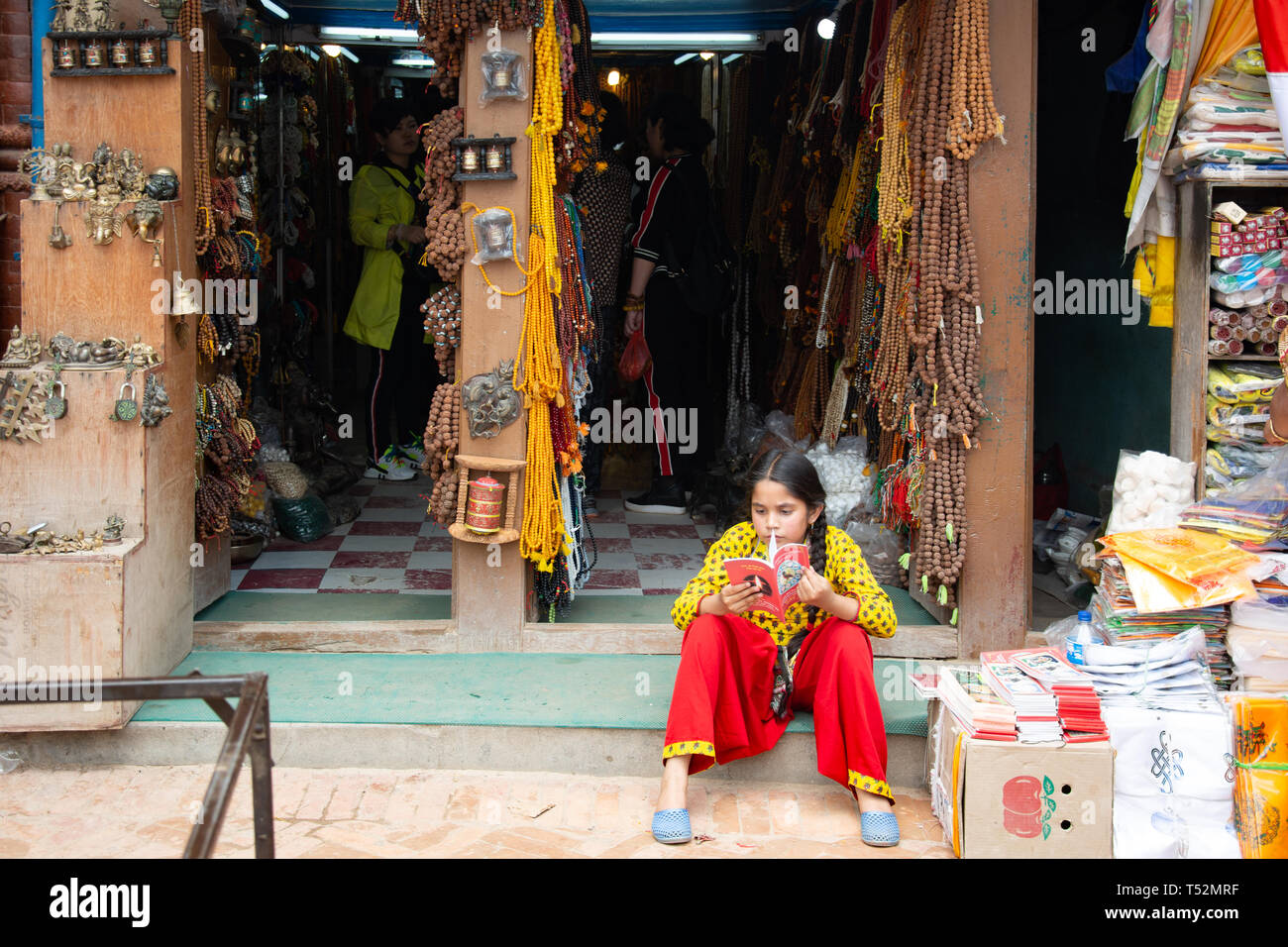 Kathmandu, Nepal - 10 Maggio 2017: una giovane ragazza si vede la lettura in attesa per i clienti di fronte a un negozio di articoli di spirituale e artefatti. Foto Stock
