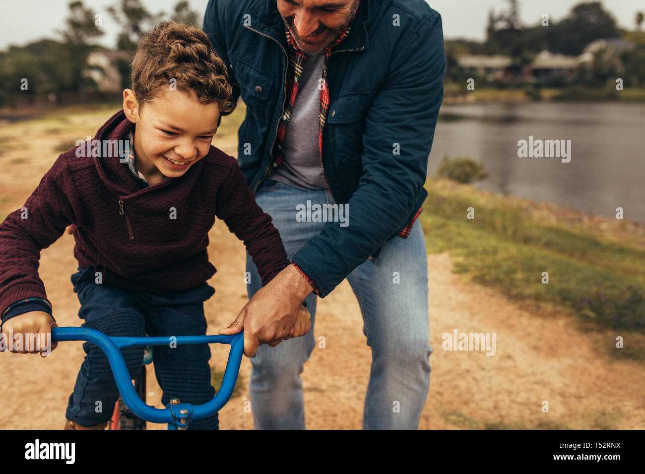 L'uomo aiutando il suo figlio per imparare ad andare in bicicletta. Emozionato kid imparare ad andare in bicicletta con il suo padre tenendo il ciclo di cadere. Foto Stock