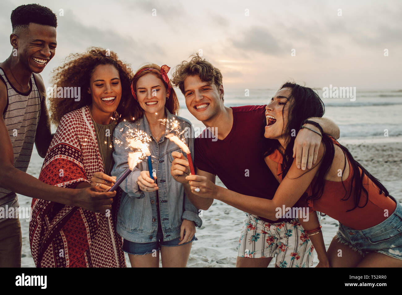 Happy amici festa sulla spiaggia con botti. Multi-etnico gruppo di amici in spiaggia in festa con fuochi d'artificio. Foto Stock