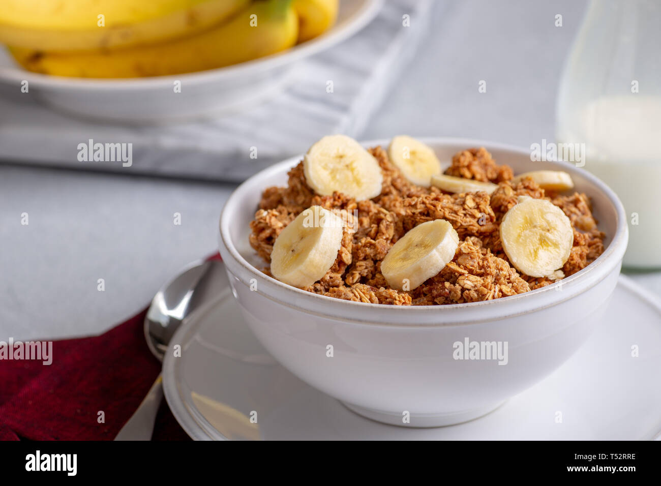 Ciotola di granola witk fette di banana e latte con le banane in background Foto Stock