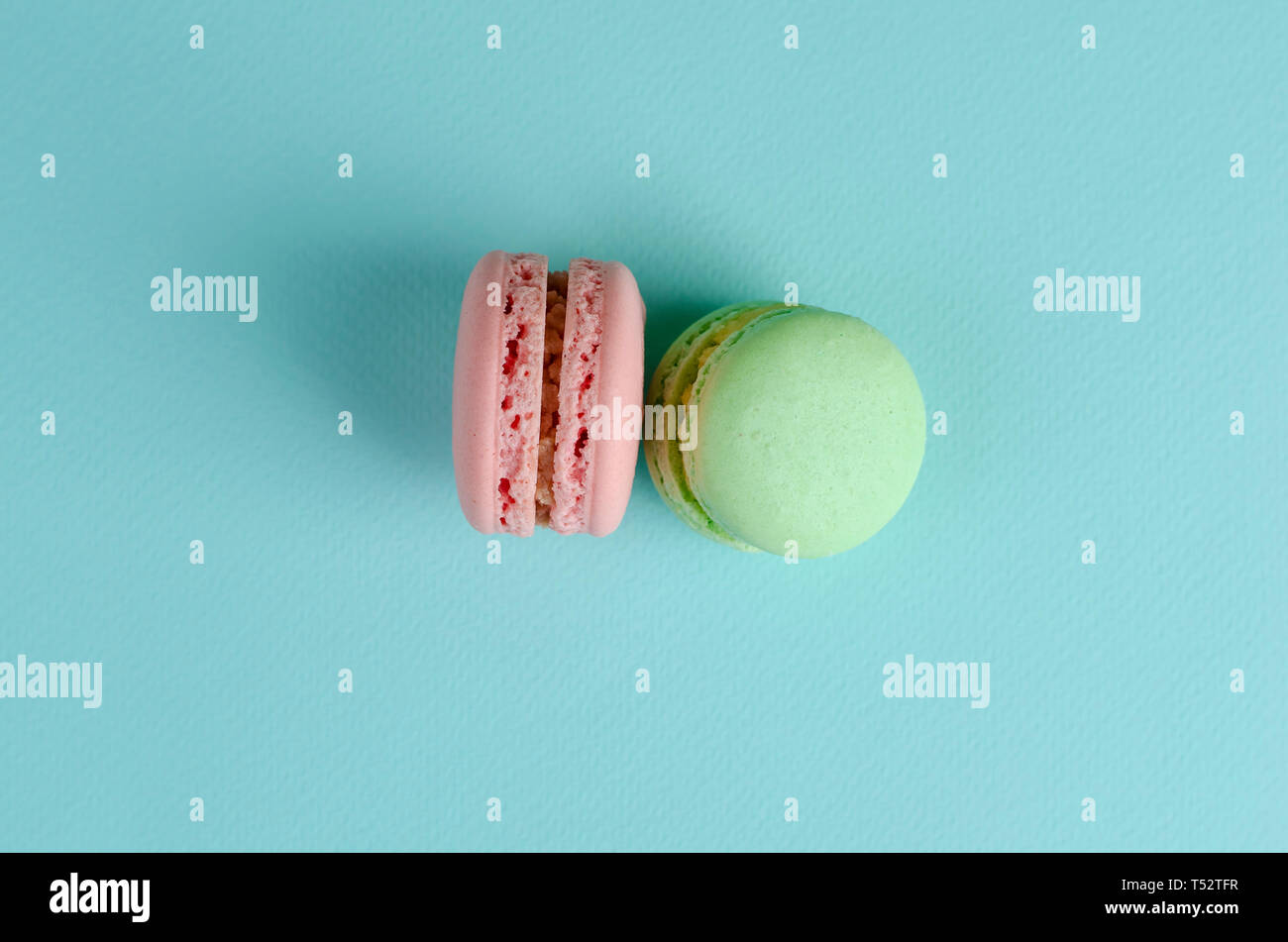 Due dolci dolci francesi di verde pastello e colori rosa amaretti o macarons pastello su sfondo blu. Spazio per il testo. Messaggio di saluto o scheda di invito Foto Stock