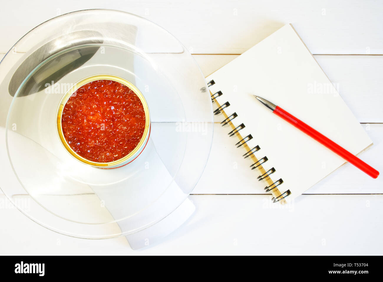 Caviale rosso in un barattolo di latta su una bilancia da cucina accanto a un blocco note. Il conteggio della quantità di proteina, calorie e grassi negli alimenti. Figura snella, fitness e prop Foto Stock