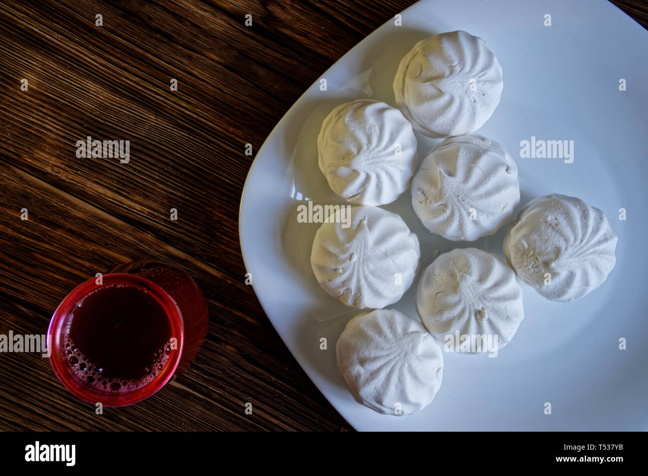 Marshmallow - zephyr consiste in una piastra su un naturale sfondo di legno di tavole di pino. Nelle vicinanze si trova un bicchiere di cacao. La luce diurna Foto Stock