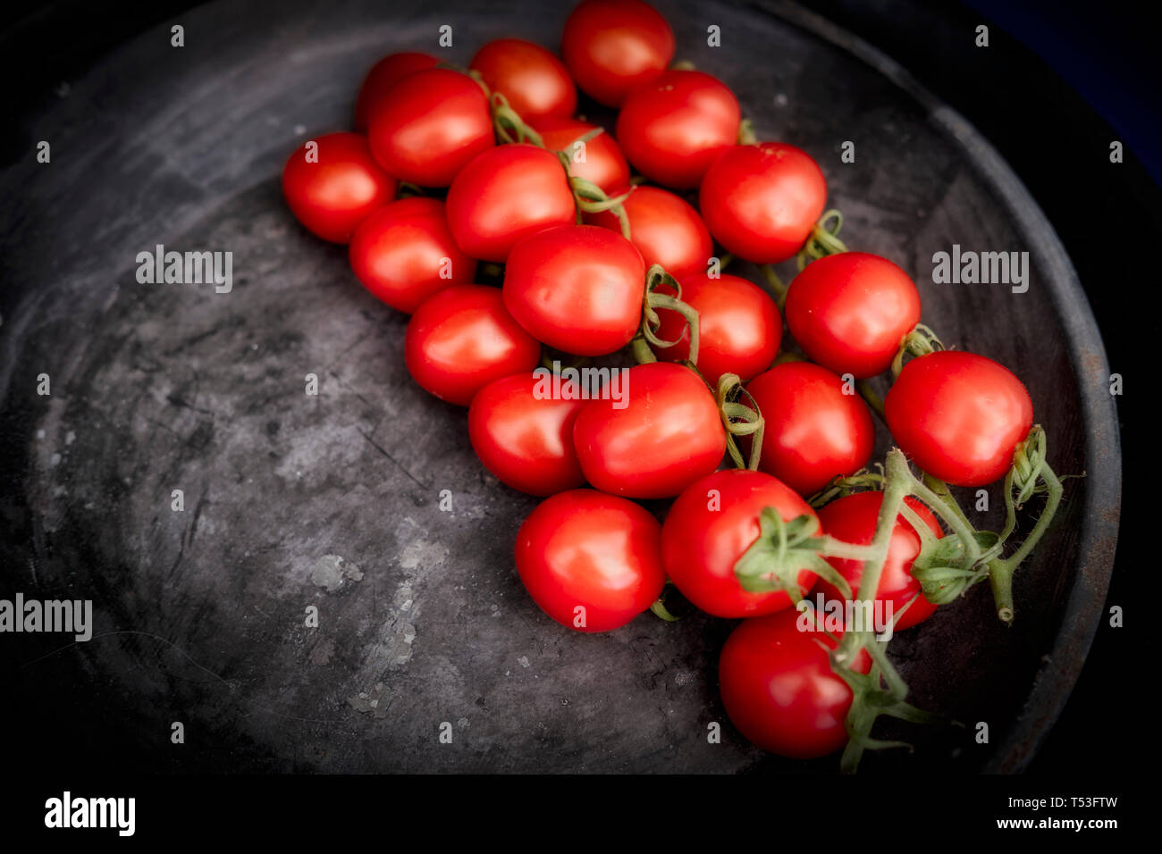Un cluster di rossi pomodori ciliegini su un vassoio nero Foto Stock