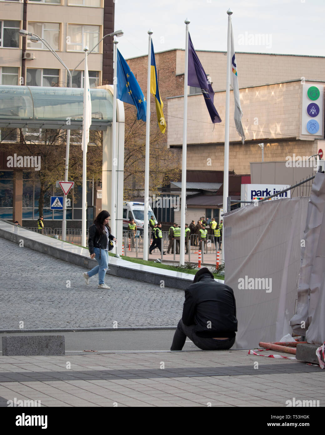 Stanco uomo seduto sulla scalinata vicino la bandiera europea insieme a Kyiv Olympiyskiy Stadium al dibattito presidenziale evento. Folla e corpi di polizia in azione. Foto Stock
