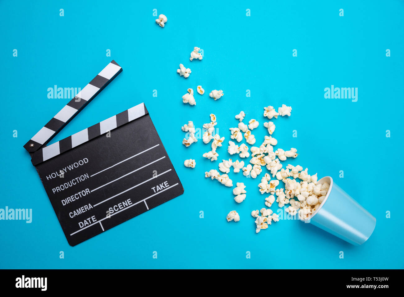 Cinema concetto. Salate fresche pop corn versato fuori da un contenitore di cartone e movie clapper board, blu colore di sfondo, vista dall'alto Foto Stock