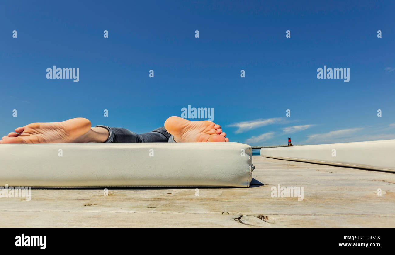 Le suole del giovane uomo con i piedi sul materasso bianco con cielo blu in background Foto Stock