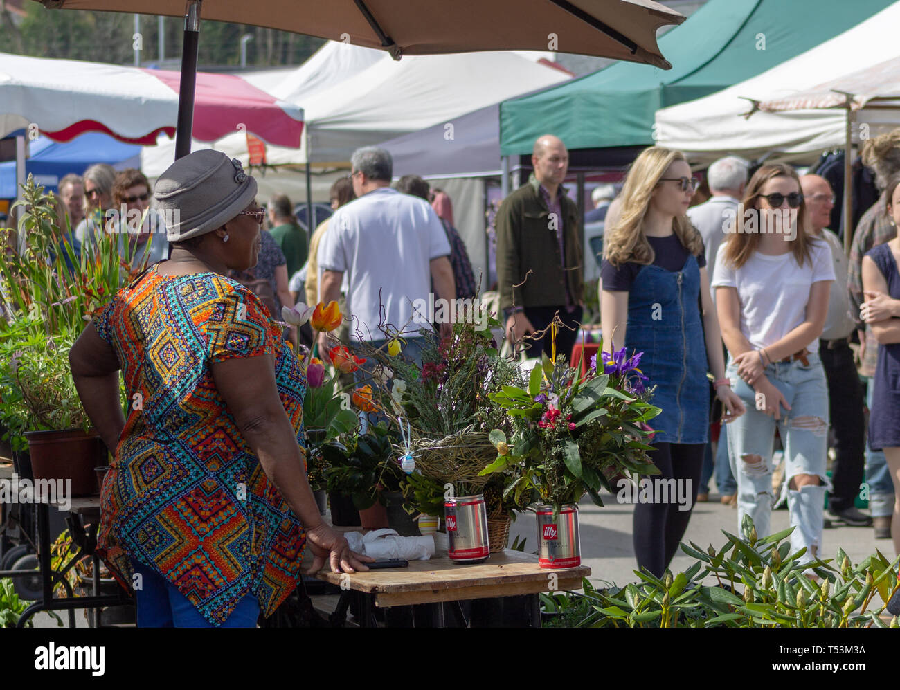 Donna in vivacemente colorato abito fiori di vendita in un mercato di un paese. Foto Stock