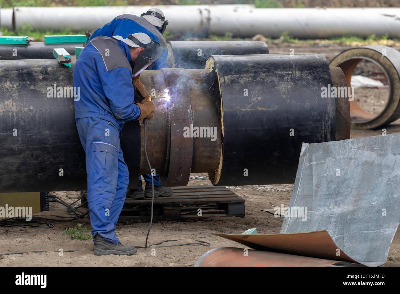Saldatrici giunti di saldatura su grandi isolati del distretto di acciaio tubo di riscaldamento con saldatura elettrica. Indossando gli ingranaggi di sicurezza. Foto Stock