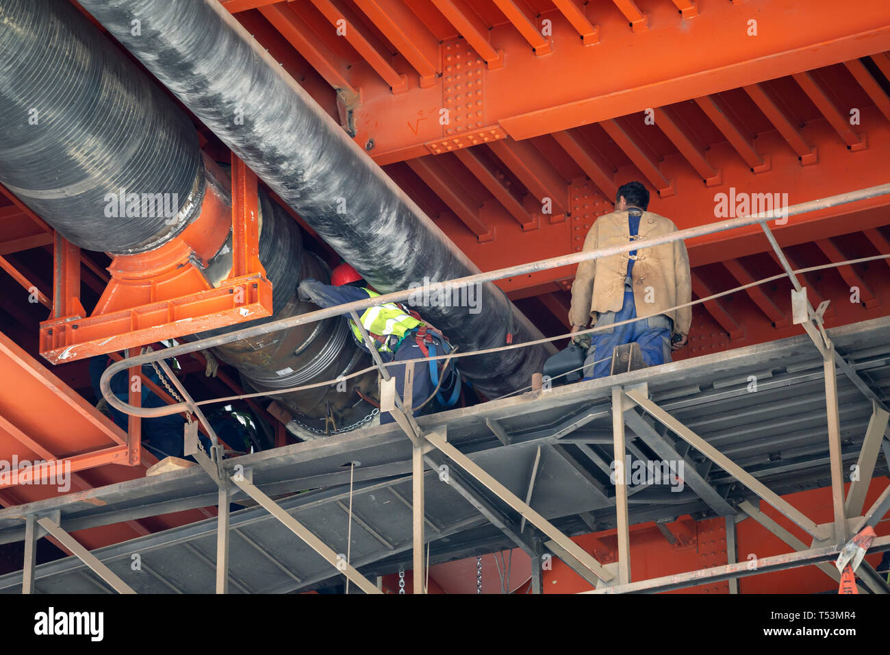 I lavoratori del distretto di saldatura pipeline di riscaldamento sotto il ponte di metallo. Pipeline di grandi lavori di installazione. Foto Stock