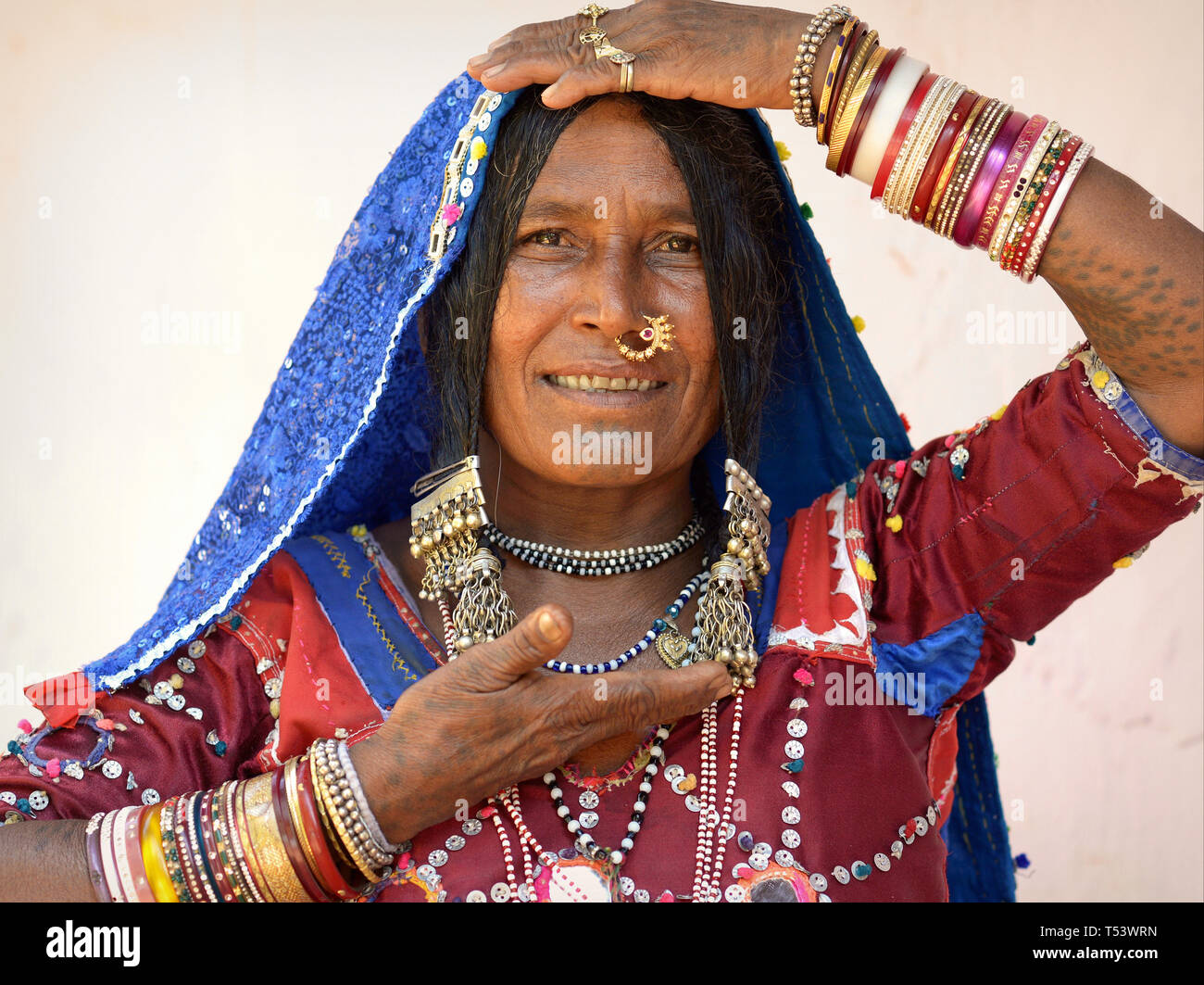 Anziani Lambadi indiano donna (Banjara, Indian gypsy) da Karnataka pone nel suo vestito tradizionale per la telecamera e mostra il suo schiave. Foto Stock
