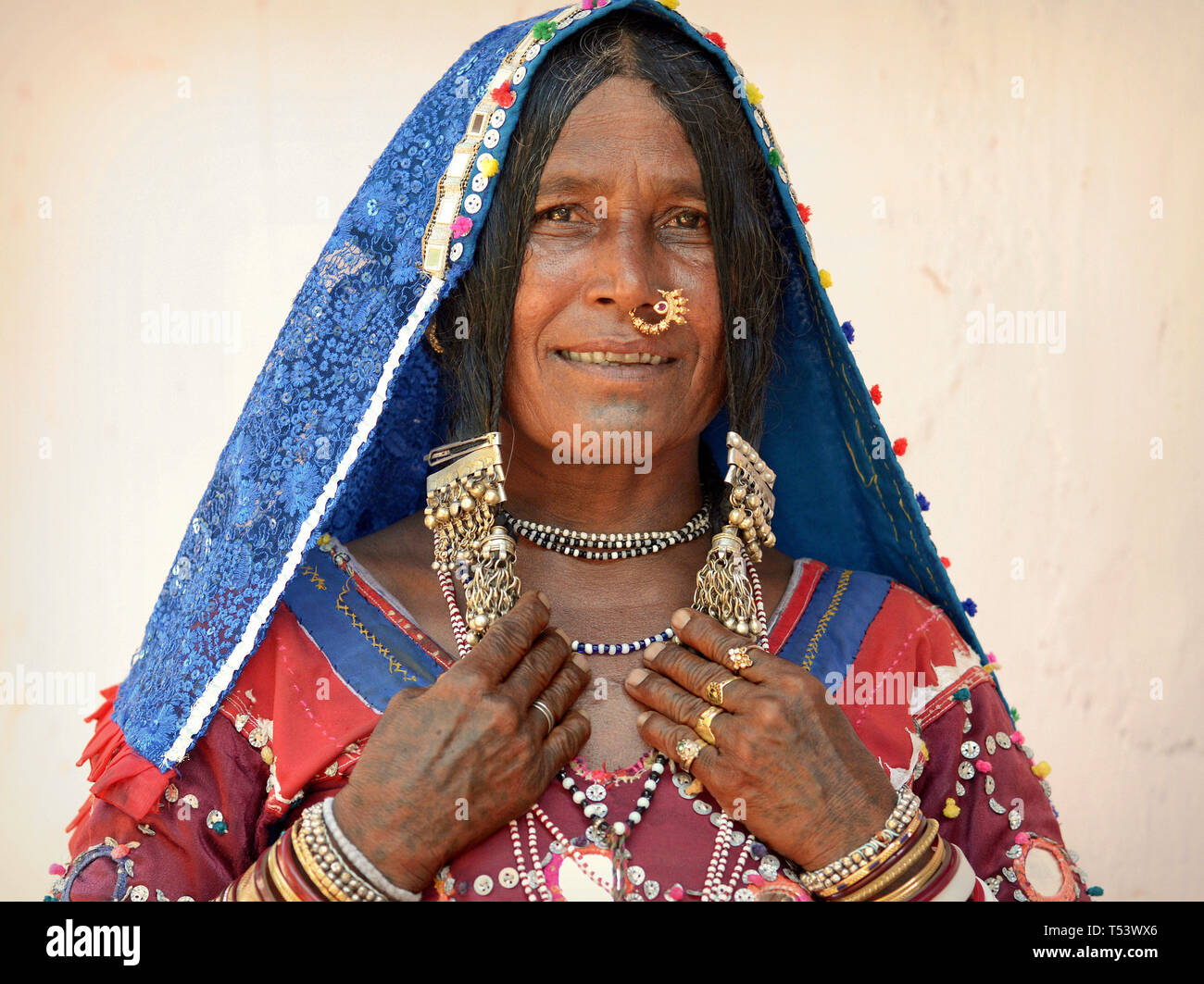 Anziani Lambadi indiano donna (Banjara, Indian gypsy) da Karnataka pone nel suo vestito tradizionale per la telecamera e mostra i suoi gioielli in argento. Foto Stock