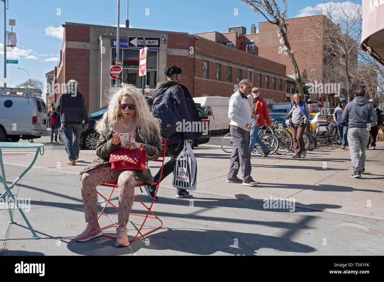 Una scena di strada con una donna seduta con lunghi capelli biondi sms sul suo telefono cellulare. In Jackson Heights, Queens, a New York City. Foto Stock