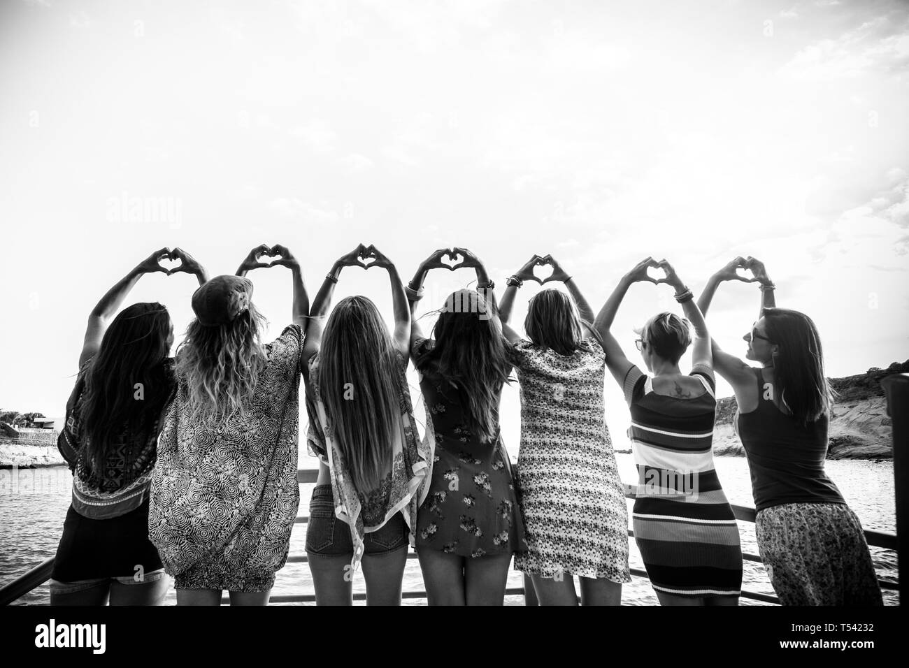Vista posteriore di un gruppo di sette persone che fanno la forma di cuore con le mani. Le donne in amicizia Foto Stock