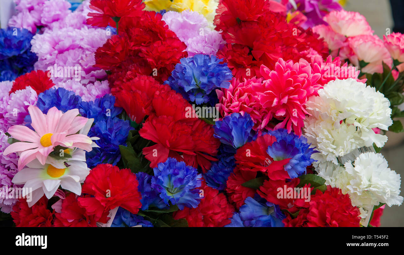 Una colorata serie di di fiori di plastica sul display al di fuori di un negozio locale. Foto Stock