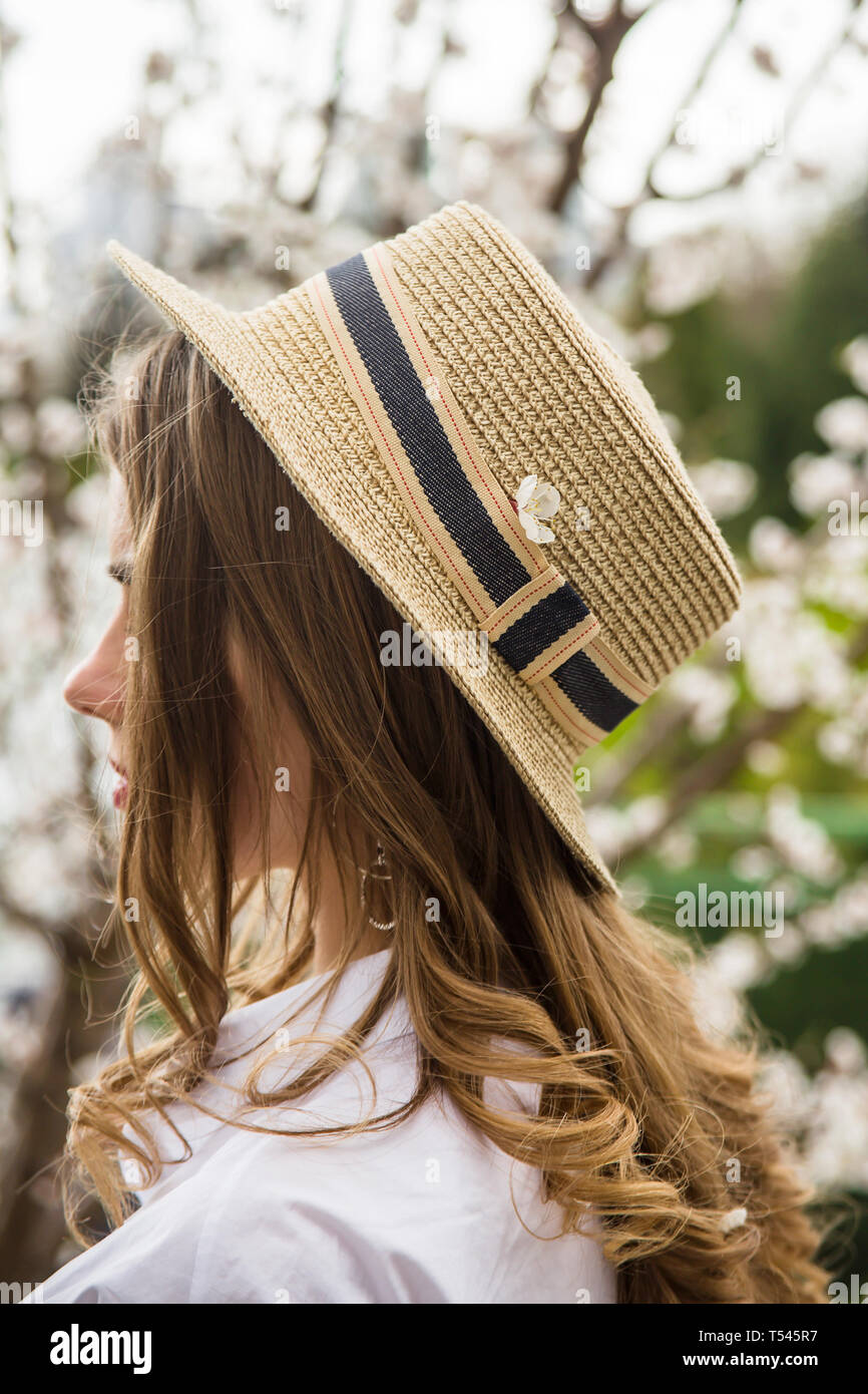 Una giovane bella ragazza caucasica in un canote hat è in piedi con la sua schiena tra white alberi in fiore. Primavera Foto Stock