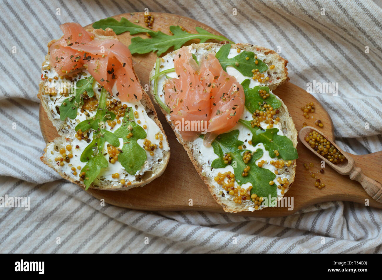 Sandwich di salmone con crema di formaggio, semi di senape e rucola sulla tavola di legno. Sana nutrizione alla moda. Colazione perfetta. Foto Stock