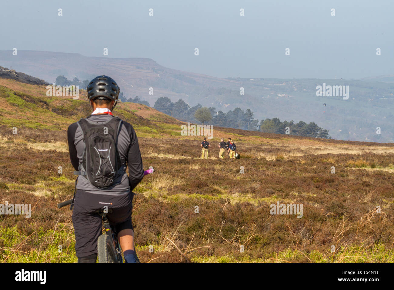 Yorkshire, Regno Unito. Xxi Aprile 2019. I vigili del fuoco continuano gli sforzi per spegnere un incendio - Giorno 2. Mountain Biker guarda nella tristezza come l'antenna elicottero antincendio inizia ad aiutare il personale di terra di spegnere le braci ancora Ilkley Moor. Credito: Rebecca Cole/Alamy Live News Foto Stock