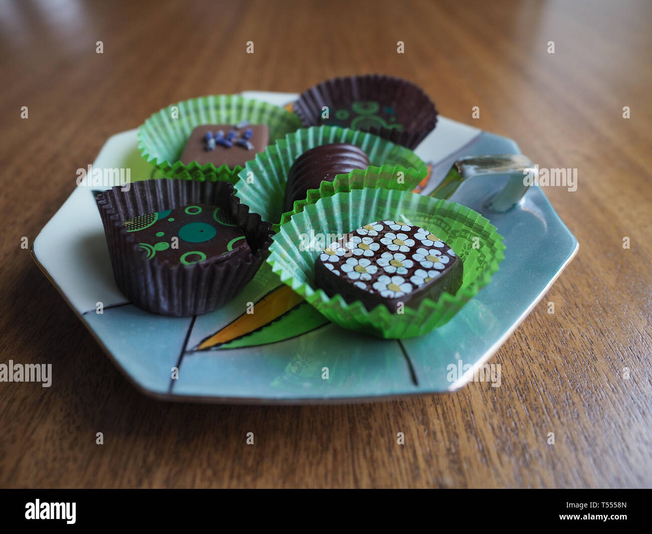 Cinque cioccolatini decorate in verde e marrone di involucri su una caramella di porcellana piatto con tavola di legno in background. Fotografato a livello degli occhi. Foto Stock