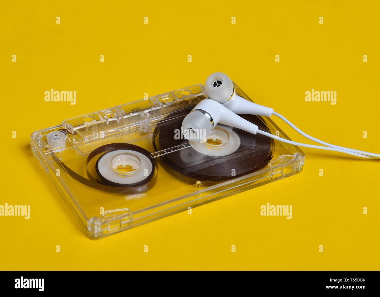 Tecnologia retrò. Plastica trasparente cassetta audio e bianco cuffie sotto vuoto su un brillante sfondo giallo. 80s. Foto Stock Tecnologia retrò. Plastica trasparente cassetta audio e bianco cuffie sotto vuoto su un brillante sfondo giallo. 80s. Foto Stock