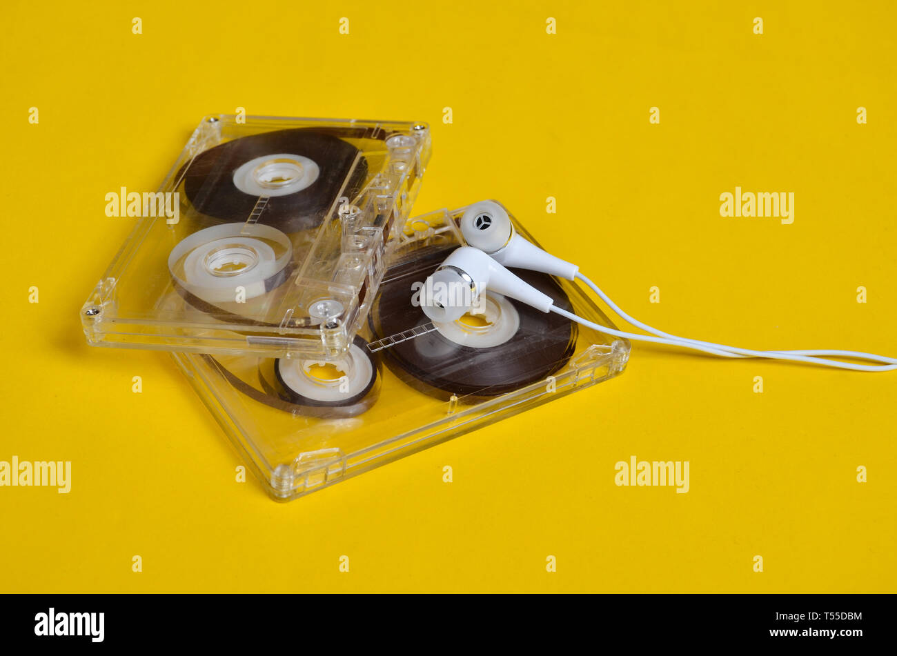 Tecnologia retrò. Plastica trasparente cassetta audio e bianco cuffie sotto vuoto su un brillante sfondo giallo. 80s. Foto Stock Tecnologia retrò. Plastica trasparente cassetta audio e bianco cuffie sotto vuoto su un brillante sfondo giallo. 80s. Foto Stock