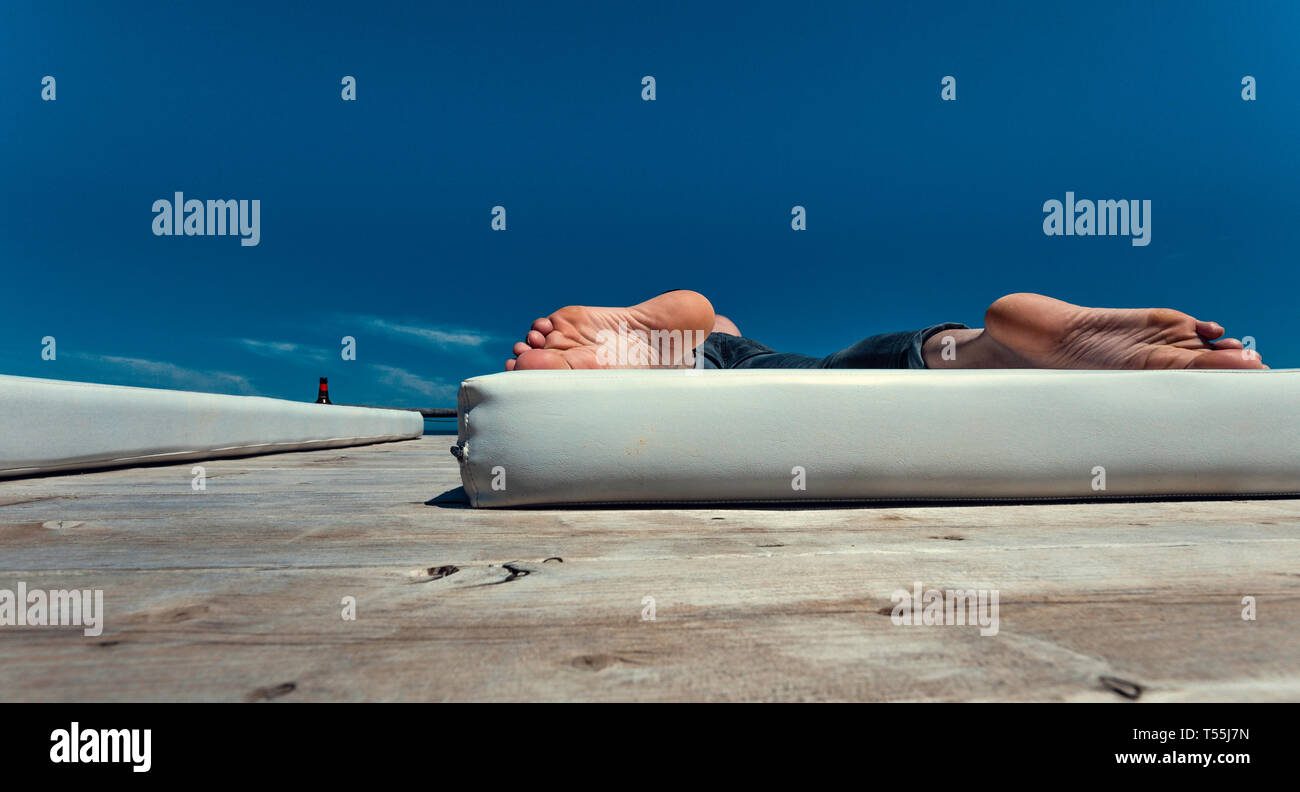 Le suole del giovane uomo con i piedi sul materasso bianco con cielo blu in background e spazio di copia Foto Stock