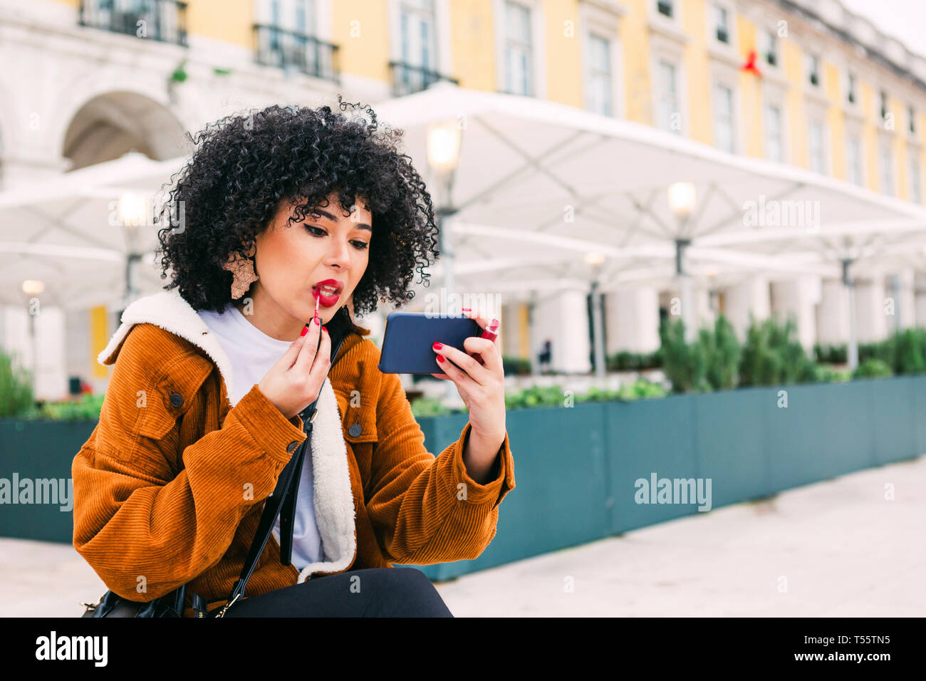 Giovane donna applicando un rossetto rosso utilizzando smart phone Foto Stock