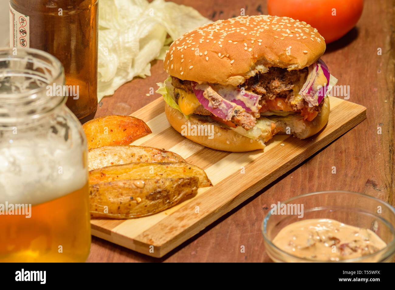 Il doppio cheeseburger e mancanti di un morso, servito con birra e Spicchi di patate spazio di copia Foto Stock