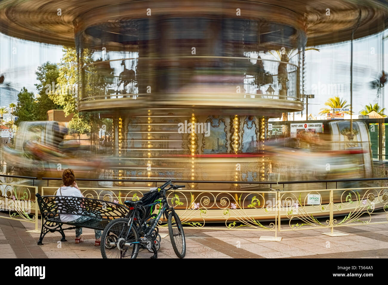 Fuengirola, Spagna - 31 giugno 2018. la giostra di movimentazione e la donna seduta sul banco accanto a una bicicletta Foto Stock
