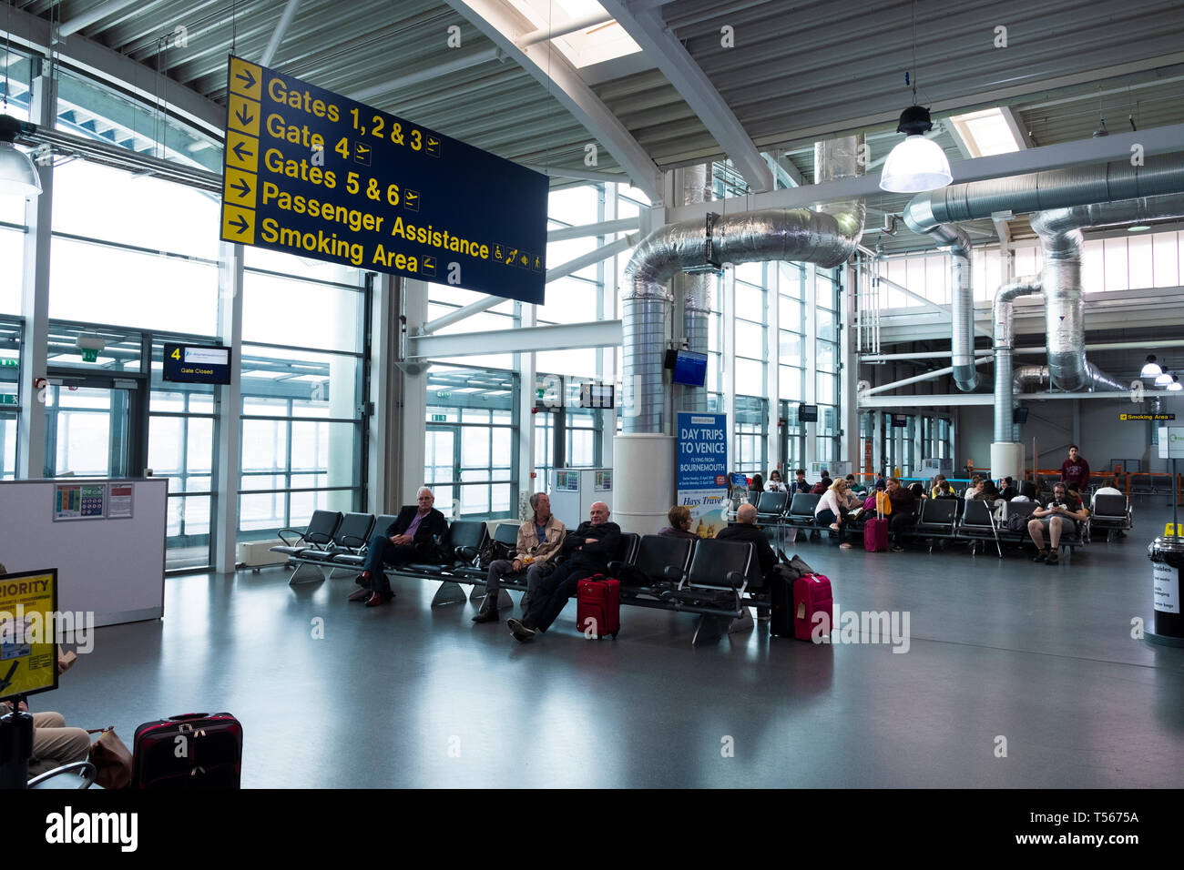 I passeggeri in attesa in aeroporto di Bournemouth sala partenze interno con segni di cancelli Foto Stock