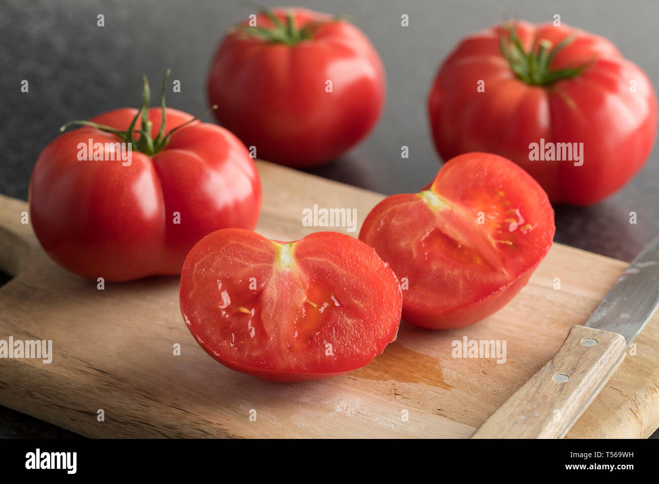 Intero e metà succosi pomodori rossi su un tagliere di legno vicino fino Foto Stock