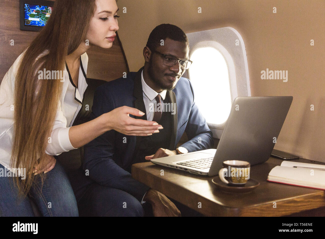 Giovani afro-americano di successo imprenditore con bicchieri e un attraente workmate femmina bionda in un jet privato. Il servizio di volo e di prima classe Foto Stock