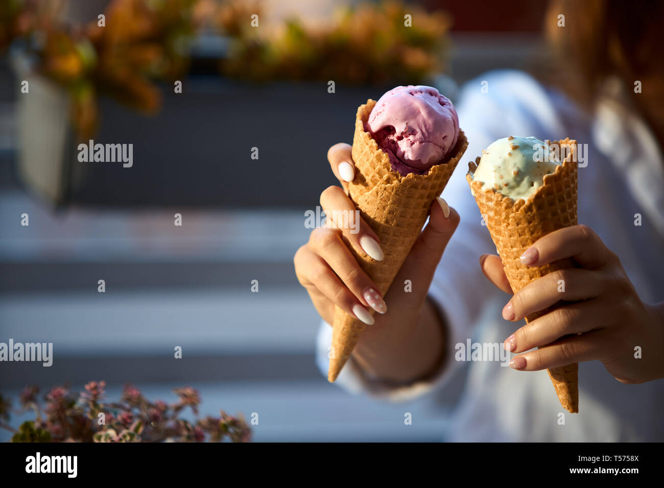 Immagine ravvicinata di coni gelato nelle mani di una donna in piedi con il suo amico. Due giovani donne all'aperto di mangiare gelato in una giornata di sole. Vista isolata, Foto Stock