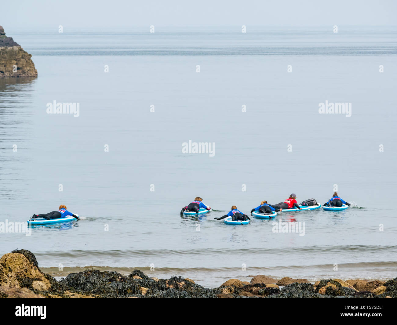 Dunbar, East Lothian, Scozia, Regno Unito. 21 apr 2019. Regno Unito: Meteo persone godono di molto soleggiata a caldo il giorno di Pasqua Il meteo a occhio grotta cove. Un gruppo di paddle boarder andare in mare per una lezione con Coast to Coast Scuola di surf Foto Stock