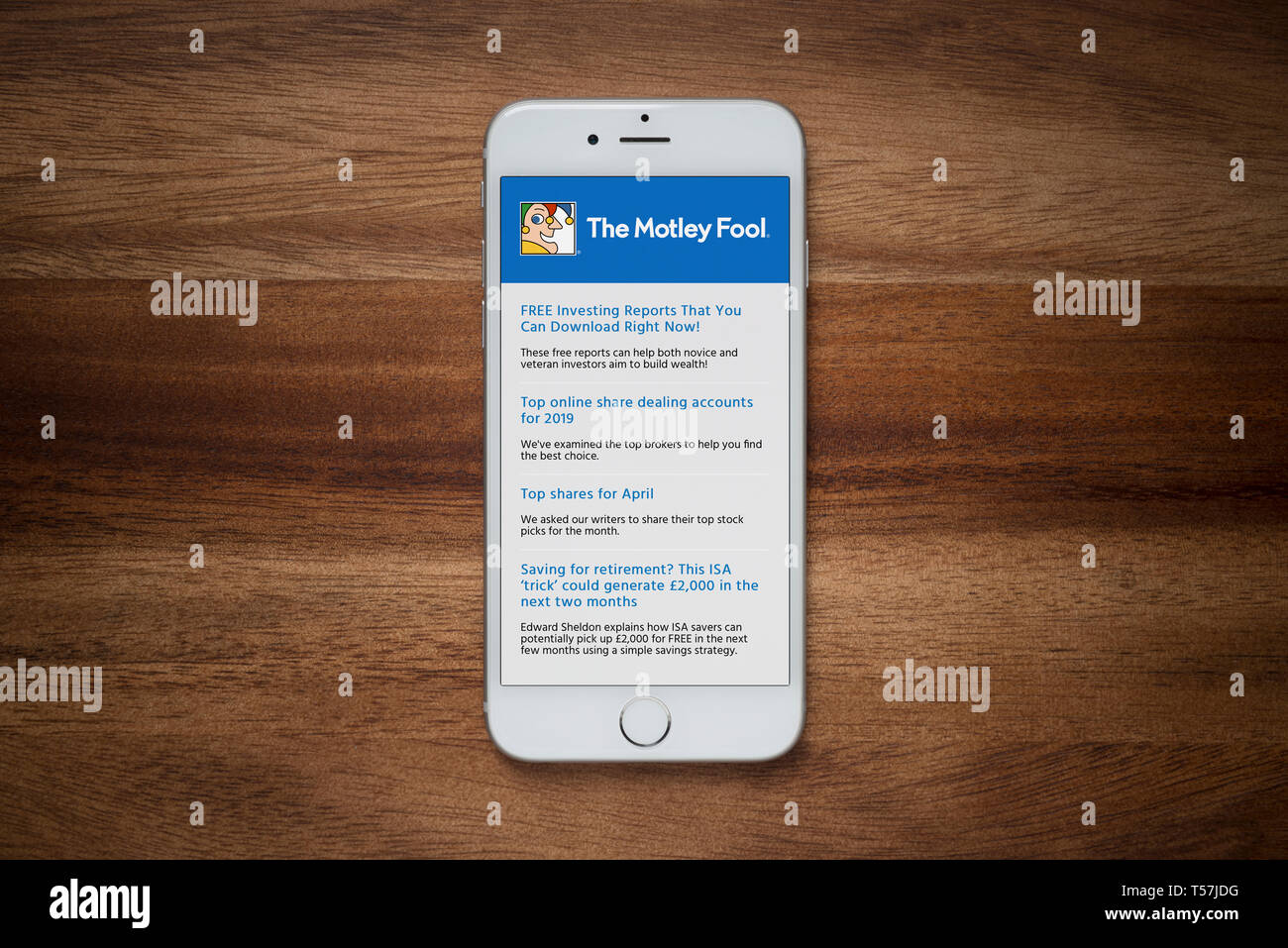 Un iPhone che mostra il Motley Fool sito poggia su una semplice tavola di legno (solo uso editoriale). Foto Stock