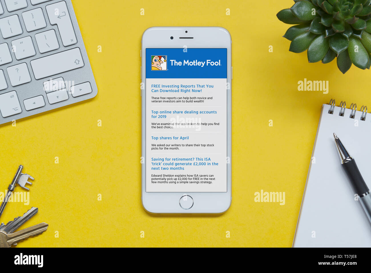 Un iPhone che mostra il Motley Fool sito poggia su uno sfondo giallo tabella con una tastiera, tasti, blocco note e di impianto (solo uso editoriale). Foto Stock