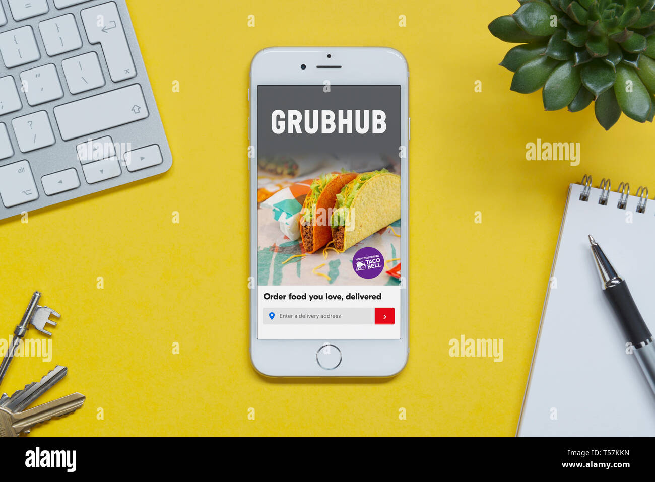 Un iPhone che mostra il sito web Grubhub poggia su uno sfondo giallo tabella con una tastiera, tasti, blocco note e di impianto (solo uso editoriale). Foto Stock