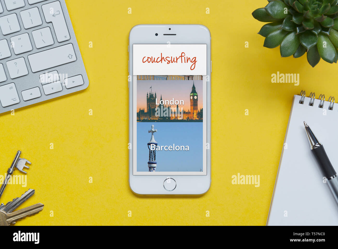 Un iPhone che mostra il sito web Couchsurfing poggia su uno sfondo giallo tabella con una tastiera, tasti, blocco note e di impianto (solo uso editoriale). Foto Stock