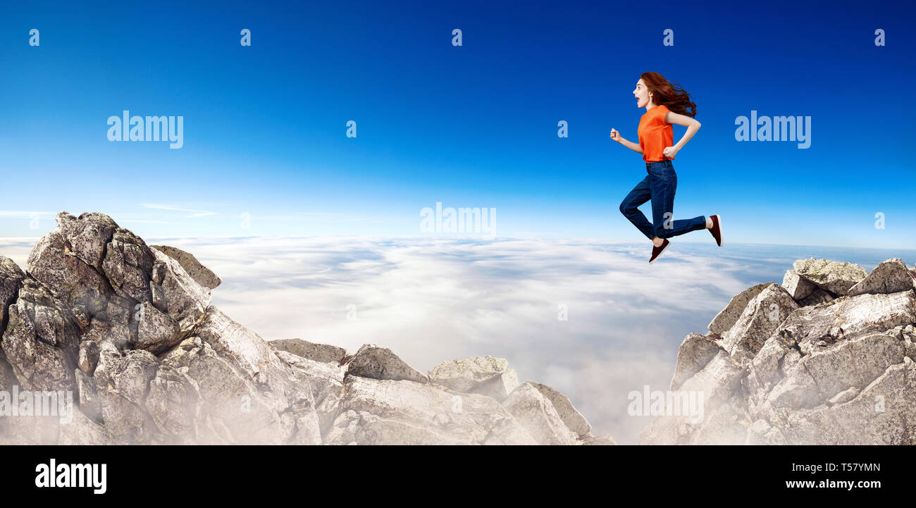 Redhead donna passa attraverso lo spazio tra le colline sulla scogliera sul cielo blu sullo sfondo. Foto Stock