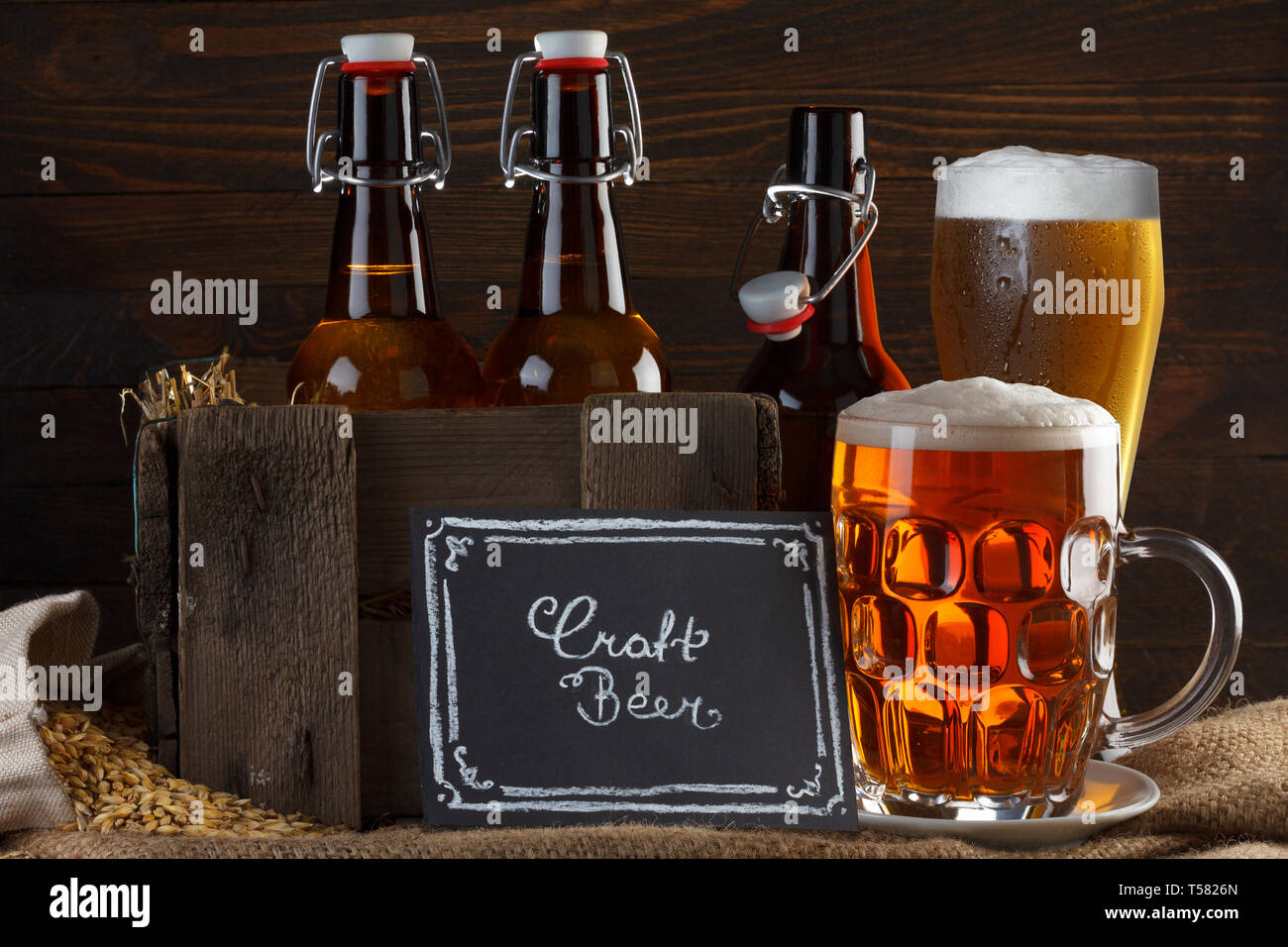 La birra artigianale in vetro e vintage gabbia in legno con bottiglie di birra su tela panno con semi di orzo Foto Stock