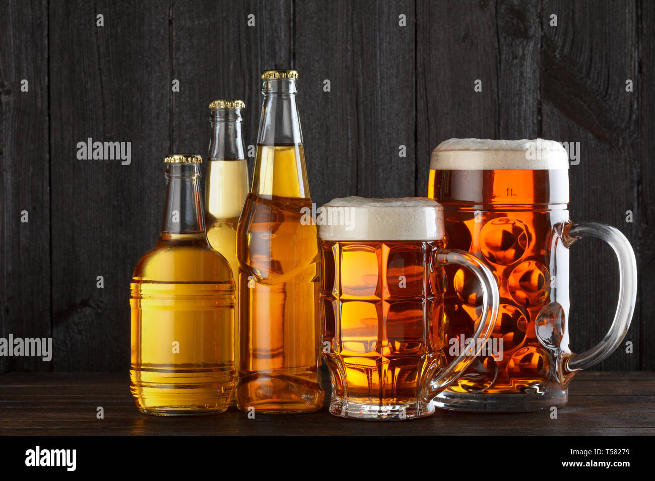 Assortimento di bicchieri e bottiglie sul tavolo, scuro dello sfondo in legno Foto Stock