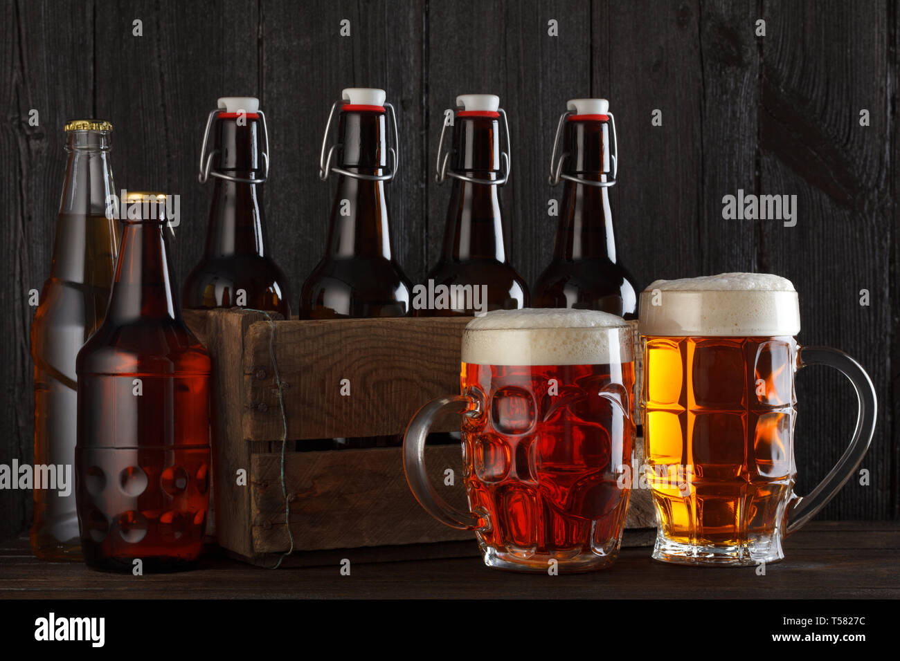 Bicchieri da birra sul tavolo con cassa piena di bottiglie, scuro dello sfondo in legno Foto Stock
