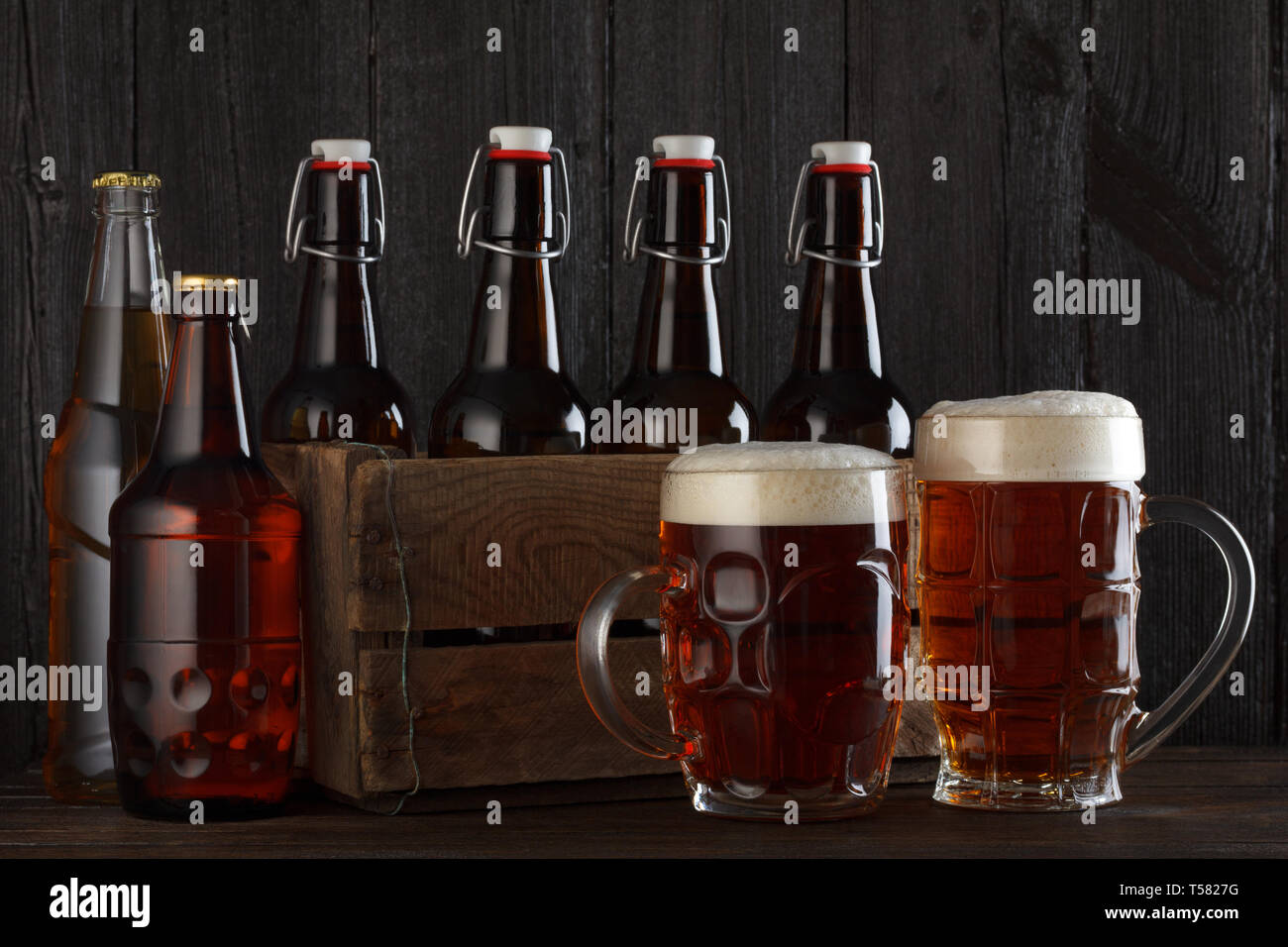 Bicchieri da birra sul tavolo con cassa piena di bottiglie, scuro dello sfondo in legno Foto Stock