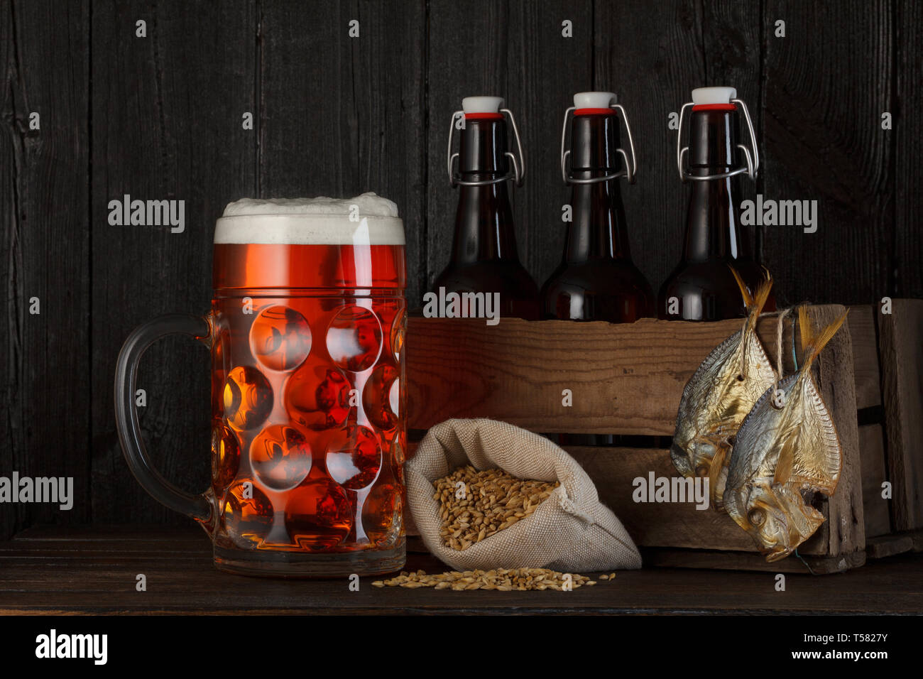 Bicchiere di birra sul tavolo con gabbia in legno pieno di bottiglie, il sacchetto con la birra di orzo e salato pesce essiccato Foto Stock