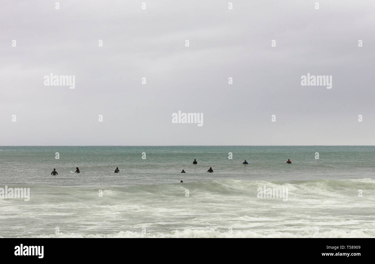 Surfers sui tavoli in attesa l'onda in un inverno nuvoloso giorno indossano un nero tuta in neoprene, spazio libero per il testo sulla parte superiore Foto Stock