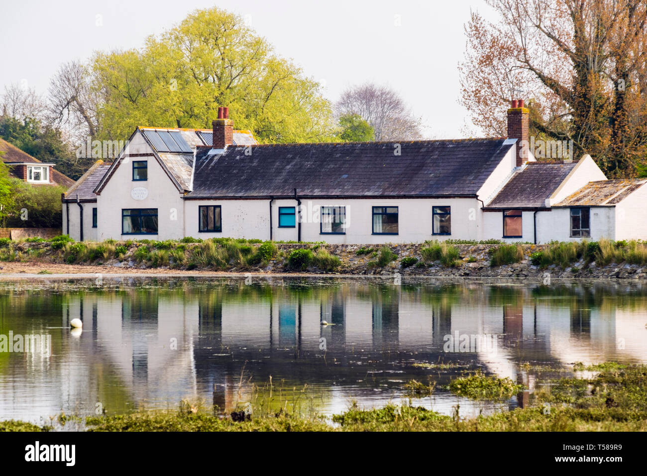 La Scuola nazionale 1834 convertito in una casa si riflette nel torrente a marea alta. Bosham, Chichester, West Sussex, in Inghilterra, Regno Unito, Gran Bretagna Foto Stock