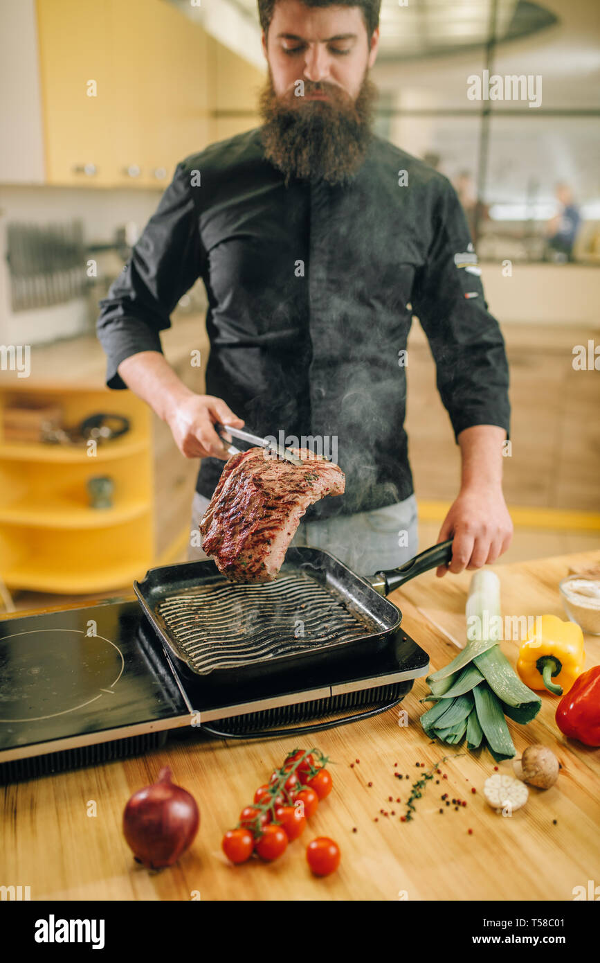Persona di sesso maschile la cottura della carne in una padella in cucina Foto Stock