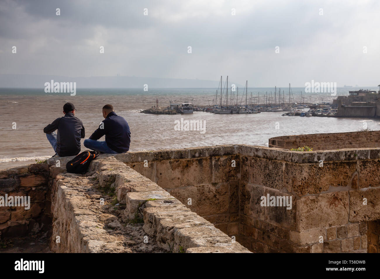 Acre, distretto del Nord, Israele - Aprile 1, 2019: giovane amici sono seduti sulla parete della città dal mare mediterraneo presso la vecchia città di Akko durante un cl Foto Stock