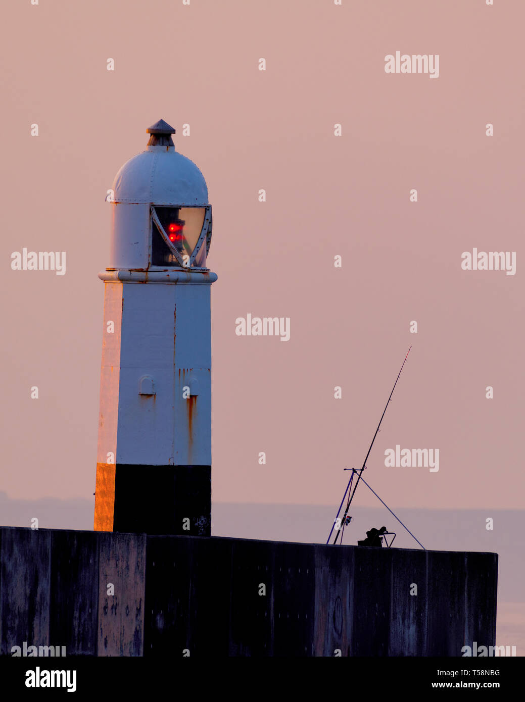 Una canna da pesca e stand silhouette contro il cielo di alba a Porthcawl faro UK. Foto Stock