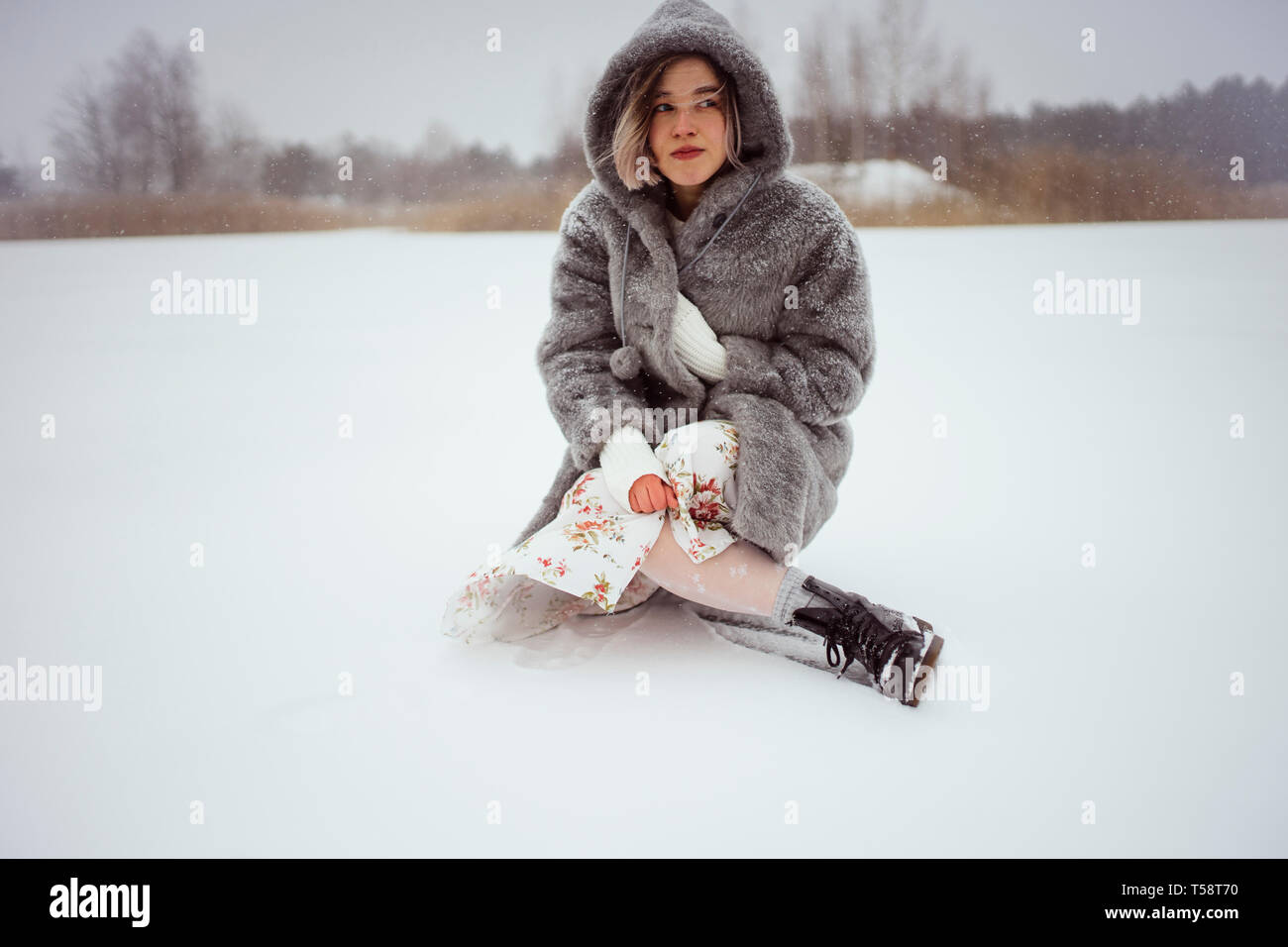 Una donna in pelliccia si siede su un lago innevato in inverno Foto Stock